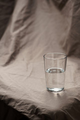 Composition glass cup half filled with water on a cloth background. Soft light.