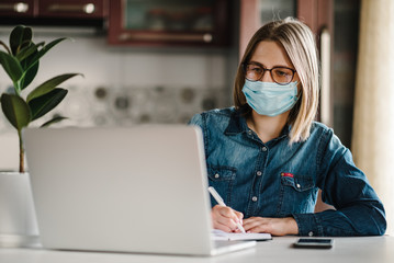 Coronavirus. Business woman working in home, wearing protective mask in quarantine. Stay at home. Girl learns, using laptop computer in home office. Freelance. Communication and technology concept.