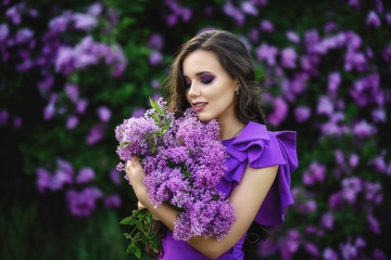 beautiful young girl in a purple dress holds in her hands a bouquet of lilac in bloom lilac.