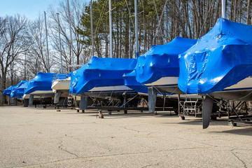 row of boats covered with blue shrink wrap in outdoor storage lot