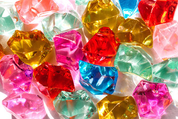 Bright multicolored transparent glass stones with the glare of the sun on a white background close...