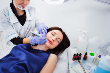 Young woman having permanent makeup on lips in beautician salon on a white background. Close up
