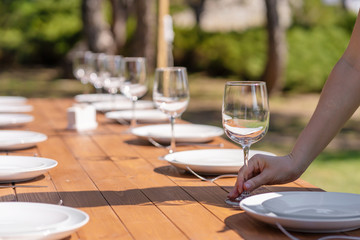 Girl the waiter in a summer cafe under the open sky arranges the dishes on a wooden banquet table.