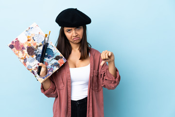 Naklejka premium Young artist woman holding a palette over isolated blue background showing thumb down with two hands.