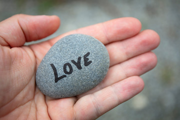 Stone with the word love written on it held in a man's hand and on an unfocused background