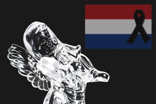 The photo of an angel with a tear in his eyes symbolizes grief over the tragedy that happened. In the background, in defocus, the flag of the Netherlands with a black mourning ribbon.