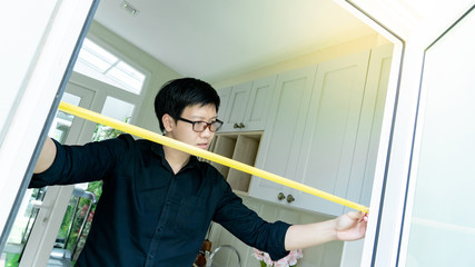 Young Asian worker man using tape measure on door frame in the kitchen. Home interior designer measuring elements on site. Housing design and construction concept