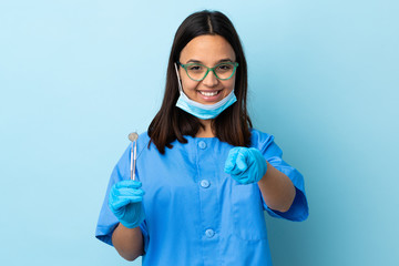 Young brunette mixed race dentist woman holding tools over isolated background making phone gesture and pointing front