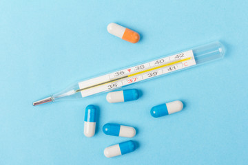 Pills isolated on blue background.Colorful medical drug capsule. Medical thermometer. Concept of coronavirus