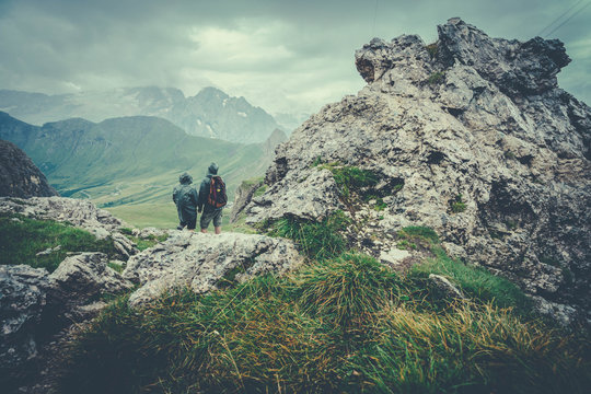 two hikers observe the valley from the top of a mountain on a cloudy day