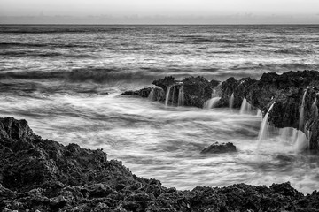 Seascape with motion blur and water flowing over the coral cliff. Blach and white