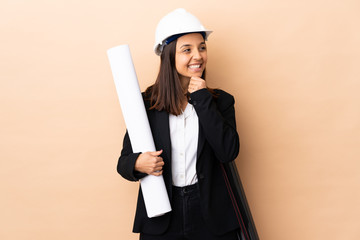 Young architect woman holding blueprints over isolated background looking to the side and smiling
