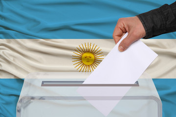 male voter drops a ballot in a transparent ballot box against the background of the national flag...