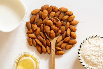Natural flour, oil and almond seed milk in a glass bowl. Nut almonds in a wooden spoon on a white background. Abstraction tree.