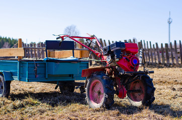 A small mini red tractor stands on a farm yard on grass and waits for work to begin. Springtime and harvest concept. new crop in isolation