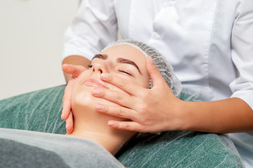 Fototapeta na wymiar Head massage of young woman by cosmetologist at beauty salon.