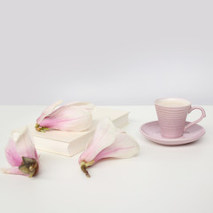 Fototapeta na wymiar cup of cappuccino on a white table, blooming magnolia buds, a book in a white cover on a delicate pink background, a blank for the designer, an invitation form, a spring mood concept
