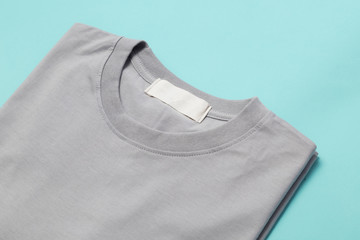 Grey folded t-shirt with blank tag for your design isolated on blue background.