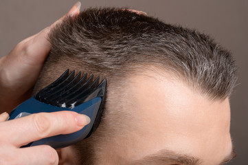 A Barber's hand with a young man's hair clipper. Creating a stylish men's haircut in a barbershop. Men's haircut process, brown tones close-up