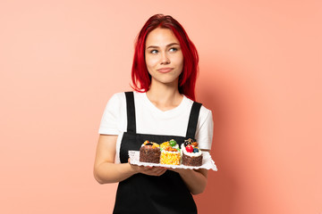 Pastry chef holding a muffins isolated on pink background scheming something