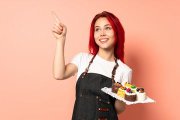 Pastry chef holding a muffins isolated on pink background pointing with the index finger a great idea