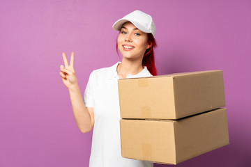 Teenager delivery girl isolated on purple background smiling and showing victory sign