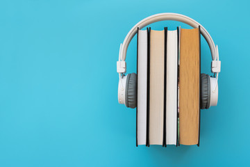 White headphones with stack of books on blue background. Audio books or modern education concept