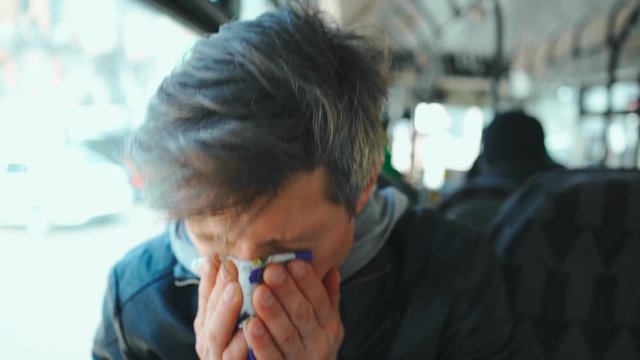 middle aged european man sneezes and Coughing while sitting in city bus. sick male in public transport without protective mask. spread of coronavirus and viral infection in public places in europe