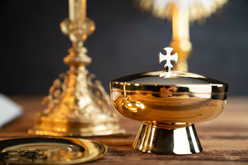 Catholic religion concept. Catholic symbols composition. The Cross, monstrance,  Holy Bible and golden chalice on wooden altar and gray background. 