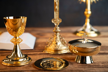 Fototapeta na wymiar Catholic religion concept. Catholic symbols composition. The Cross, monstrance, Holy Bible and golden chalice on wooden altar and gray background. 