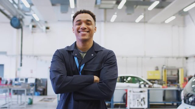 Portrait of male student studying for auto mechanic apprenticeship at college folding arms and smiling at camera - shot in slow motion