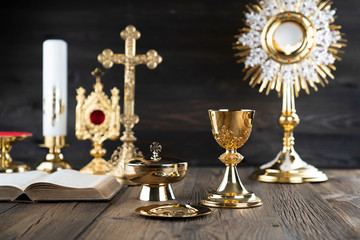 Obraz na płótnie Canvas Catholic religion concept. Catholic symbols composition. The Cross, monstrance, Holy Bible and golden chalice on wooden altar and gray background. 