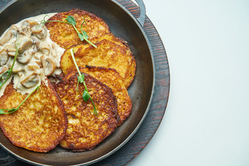 Close up view on Traditional dish of Ukrainian cuisine - potato pancakes with sour cream and mushroom in frying pan isolated on grey background