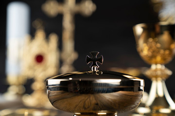 Catholic religion concept. Catholic symbols composition. The Cross, monstrance,  Holy Bible and golden chalice on wooden altar and gray background. 