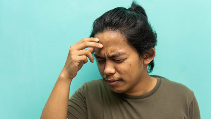 Fototapeta premium A portrait of a Malay man holding his head, having a headache with painful face reaction on isolated blue background.