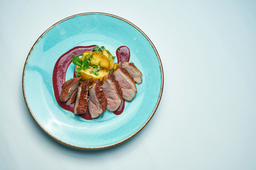 Appetizing baked sliced duck fillet with berry sauce and apples on a blue plate isolated on grey background. Close up.