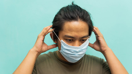 A portrait of a young Malay man wearing 3 layer surgical face mask on isolated blue background.