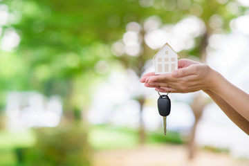Woman is holding house and car key on green