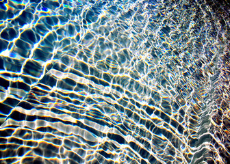 Streaming blue transparent water in swimming-pool with sunlight rays reflections 