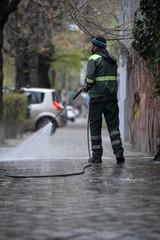 Public janitor deep cleaning the sidewalk with high pressure disinfectant solution in times of...