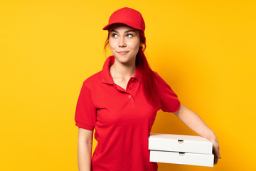 Pizza delivery girl holding a pizza over isolated background having doubts while looking up