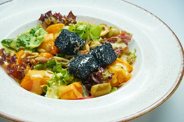 Appetizing and healthy vegetarian salad with baked pumpkin, onions, olives and cheese in sesame in white bowl isolated on grey background.