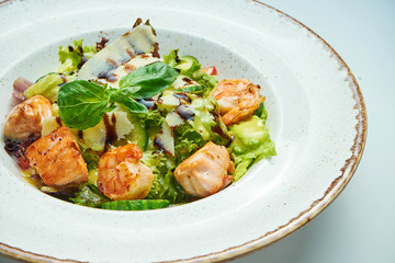 Appetizing and healthy salad with shrimp, salmon lettuce, parmesan in white bowl isolated on grey background. Seafood salad