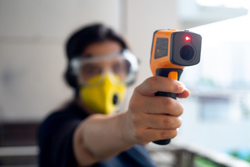 Young indian girl holding an infrared non contact thermometer to check the temperature with out of focus office residential background