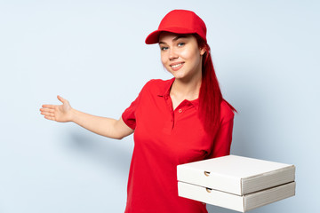 Pizza delivery girl holding a pizza over isolated background extending hands to the side for inviting to come