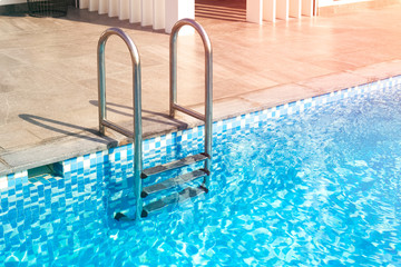 metal staircase leads to the pool. Blue water in the pool of a large house, hotel. Copy space for text