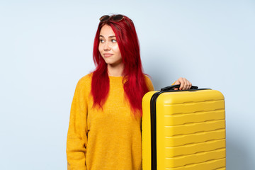 Traveler girl holding a suitcase isolated on blue background making doubts gesture looking side