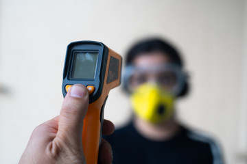 Infrared non contact thermometer being used to check an out of focus young indian girl wearing goggles and a mask