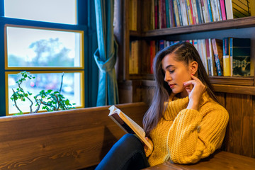 A young woman reading a book by a window