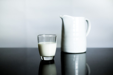 Fresh milk in a glass with white jar on black table